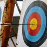 An arrow hits the bullseye on a colorful target in an indoor archery range.